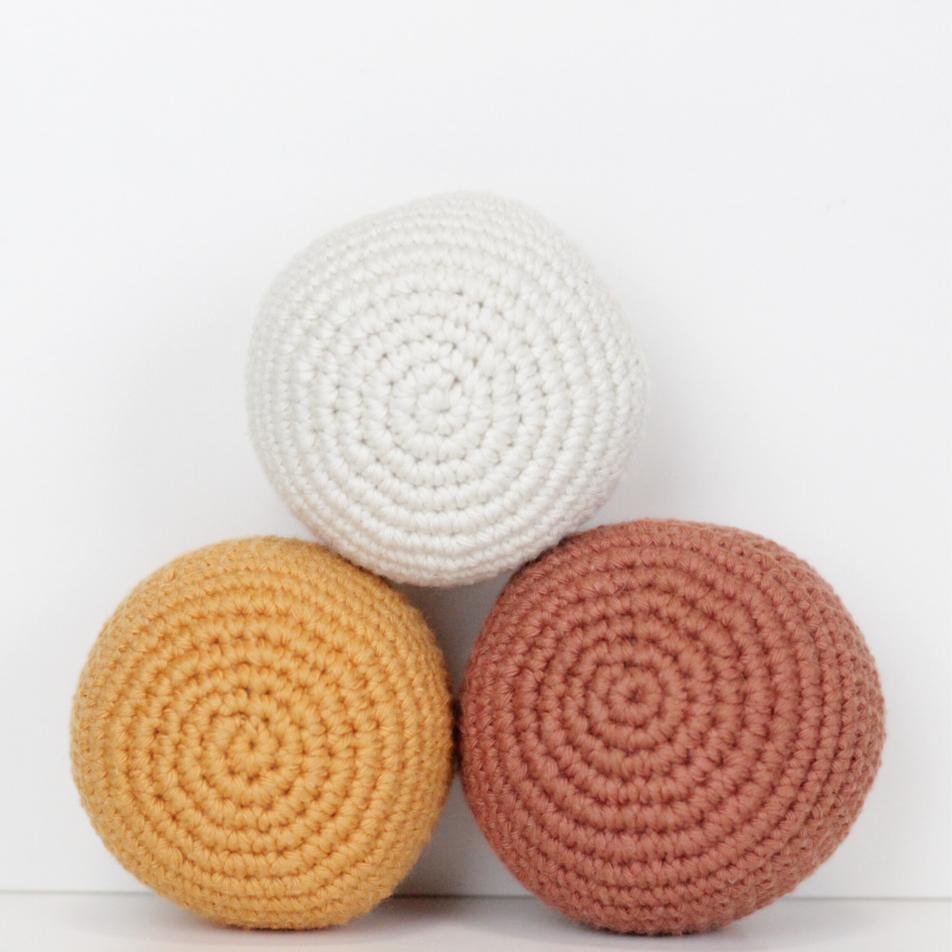 Three crocheted balls in white, rust orange, and apricot yellow. Handmade crochet dog toys from Lana Royals Pet Wear.