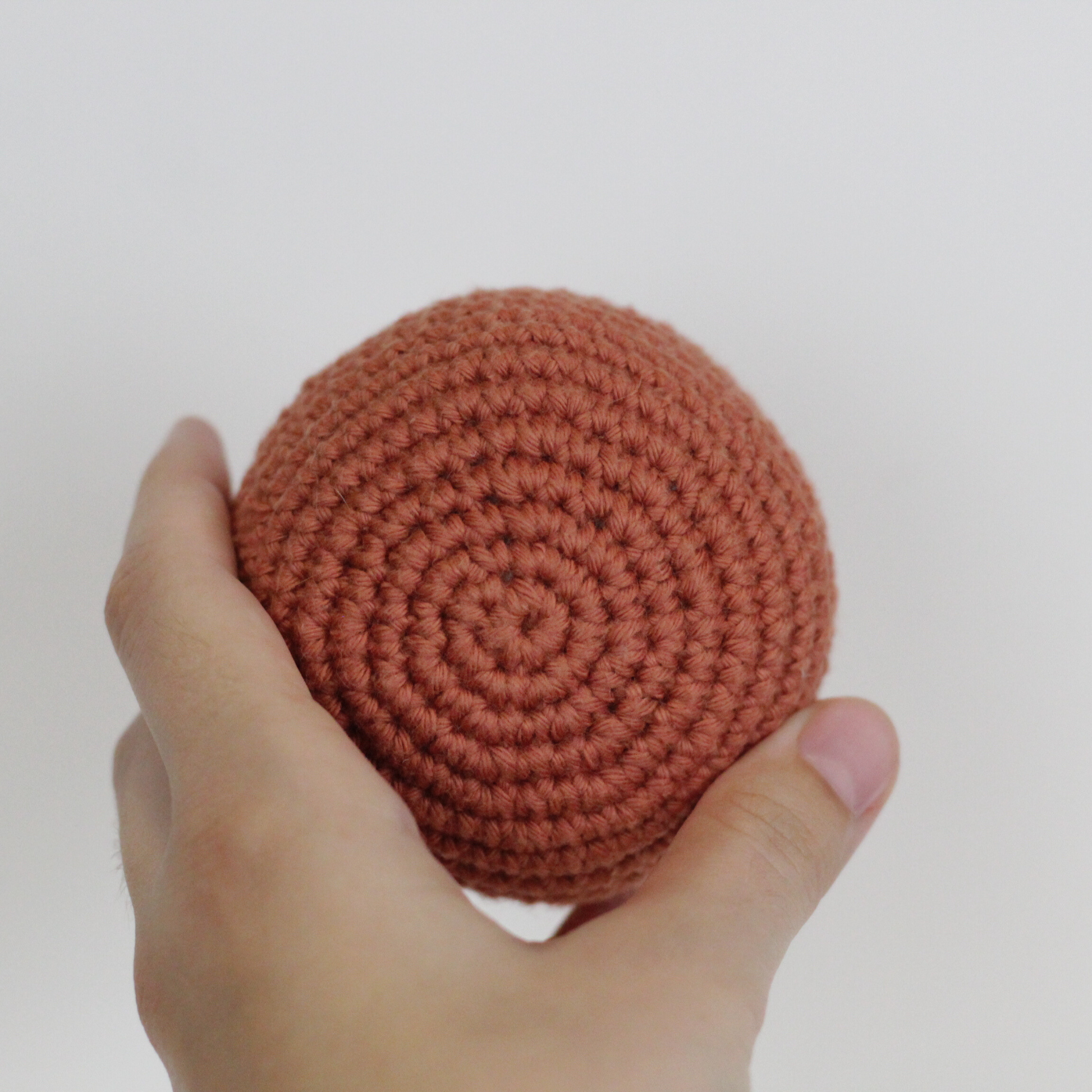 Hand holding a rust crocheted ball. Handmade crochet dog toys from Lana Royals Pet Wear.
