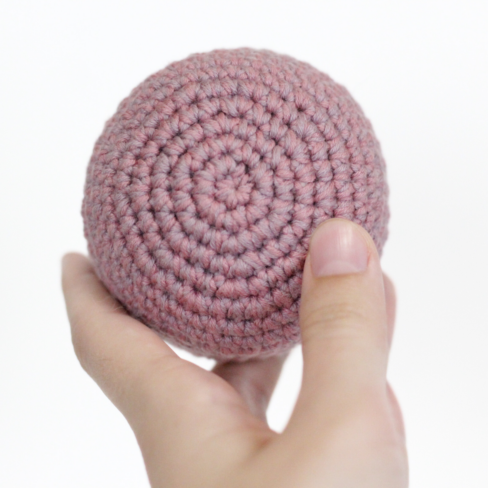 Pink crocheted ball held in a hand. Handmade crochet dog toys from Lana Royals et Wear.
