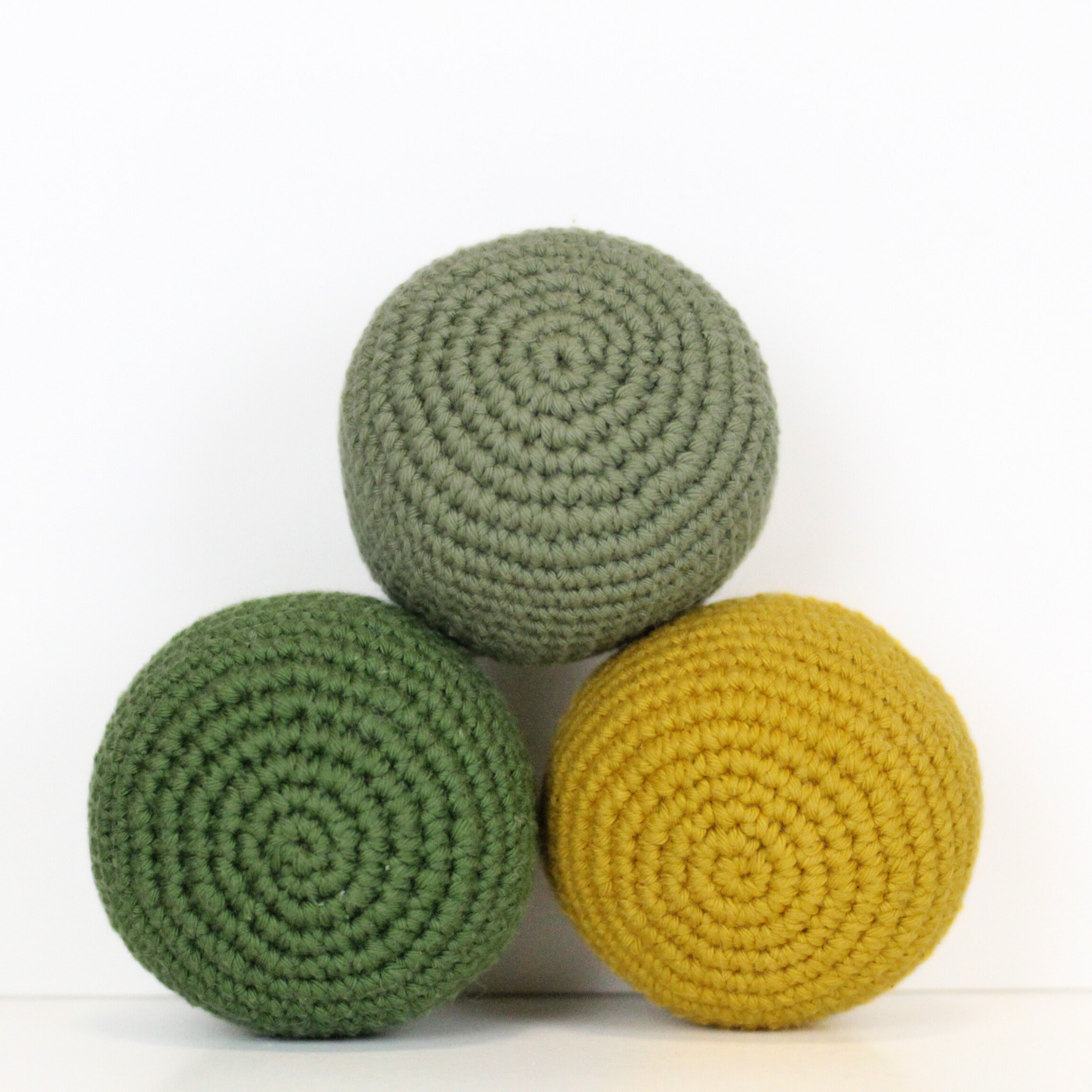 Three crocheted balls in forest green, moss green, and mustard yellow. Handmade crochet dog toys from Lana Royals Pet Wear.