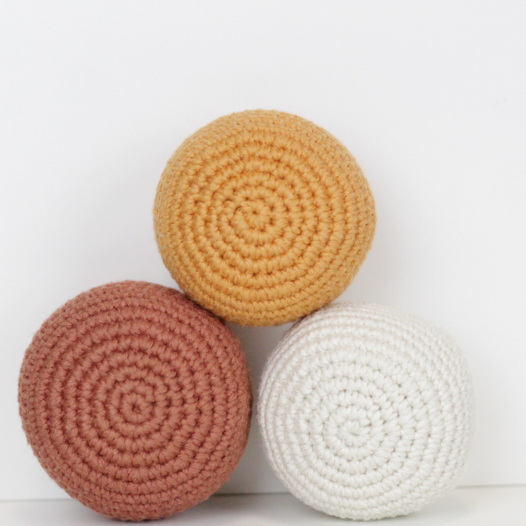 Three crocheted balls in white, rust orange, and apricot yellow. Handmade crochet dog toys from Lana Royals Pet Wear.