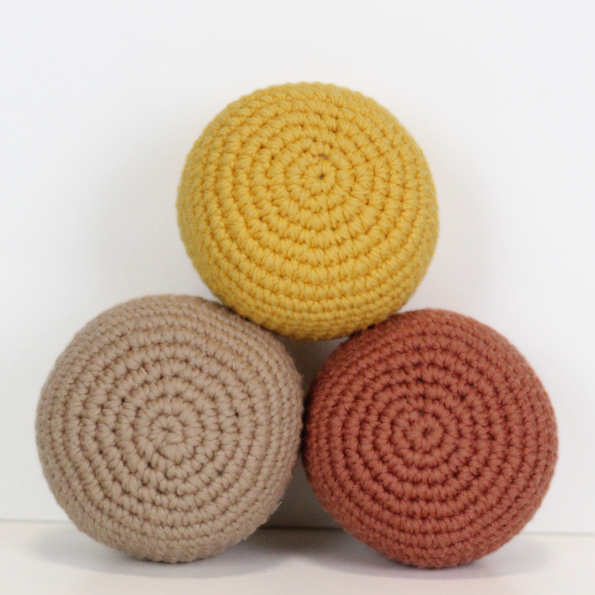 Three crocheted balls in beige, orange rust, and dandelion yellow. Three crocheted balls in forest green, moss green, and mustard yellow. Handmade crochet dog toys from Lana Royals Pet Wear.
