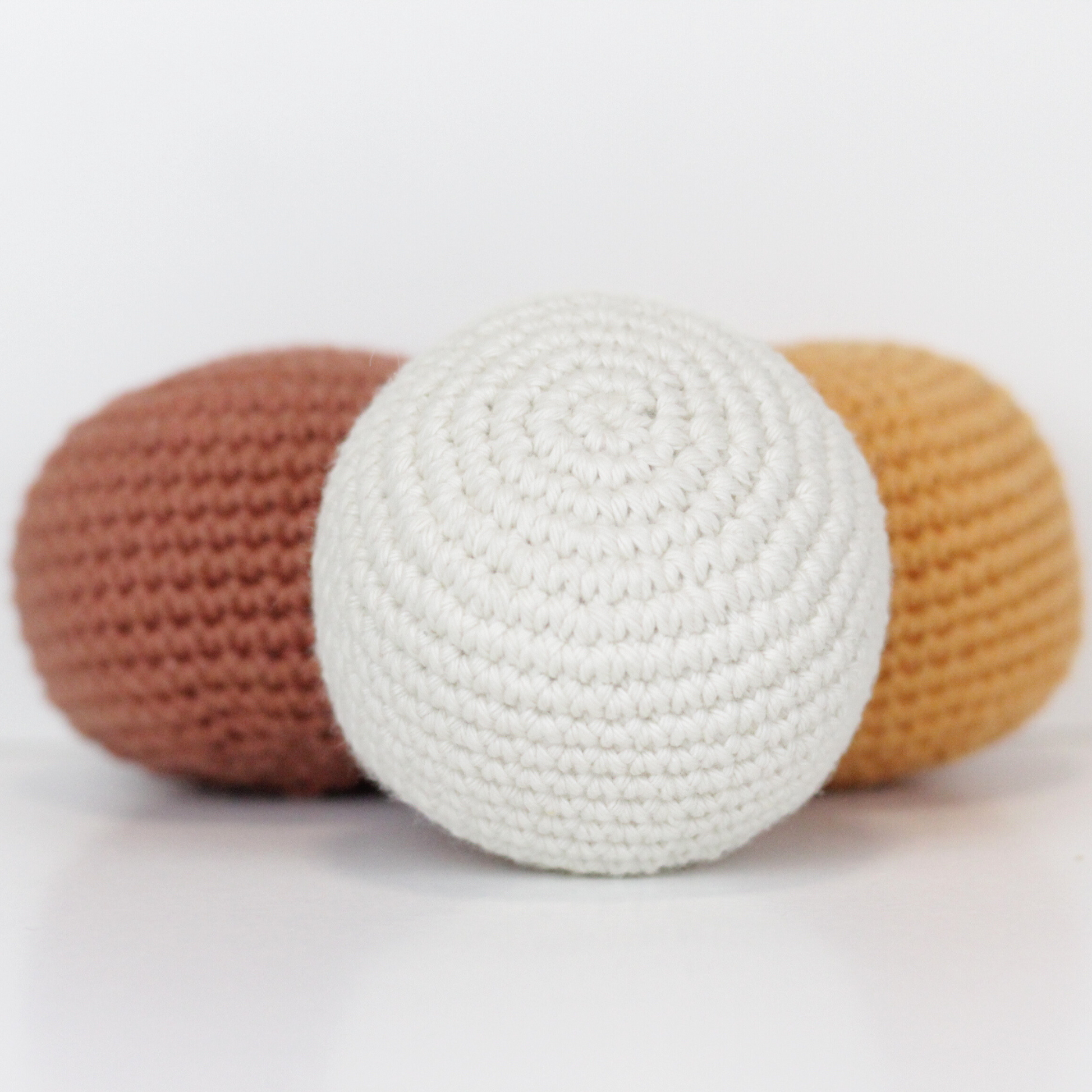 Three crocheted balls in white, rust orange, and apricot yellow. Handmade crochet dog toys from Lana Royals Pet Wear.