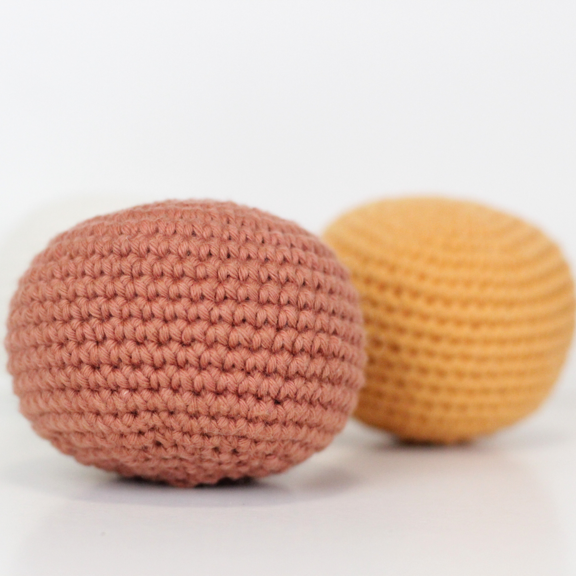 Three crocheted balls in white, rust orange, and apricot yellow. Handmade crochet dog toys from Lana Royals Pet Wear.
