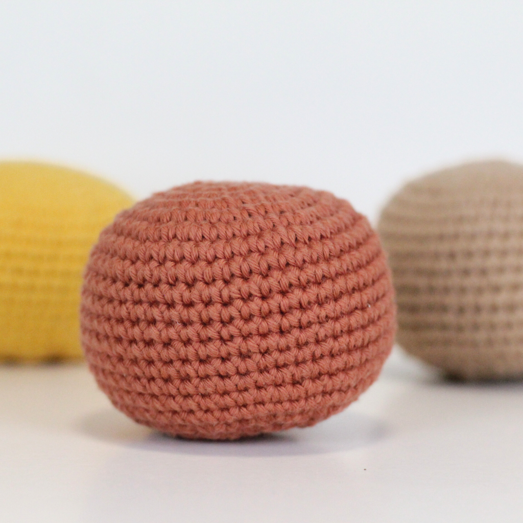 Three crocheted balls in beige, orange rust, and dandelion yellow. Three crocheted balls in forest green, moss green, and mustard yellow. Handmade crochet dog toys from Lana Royals Pet Wear.