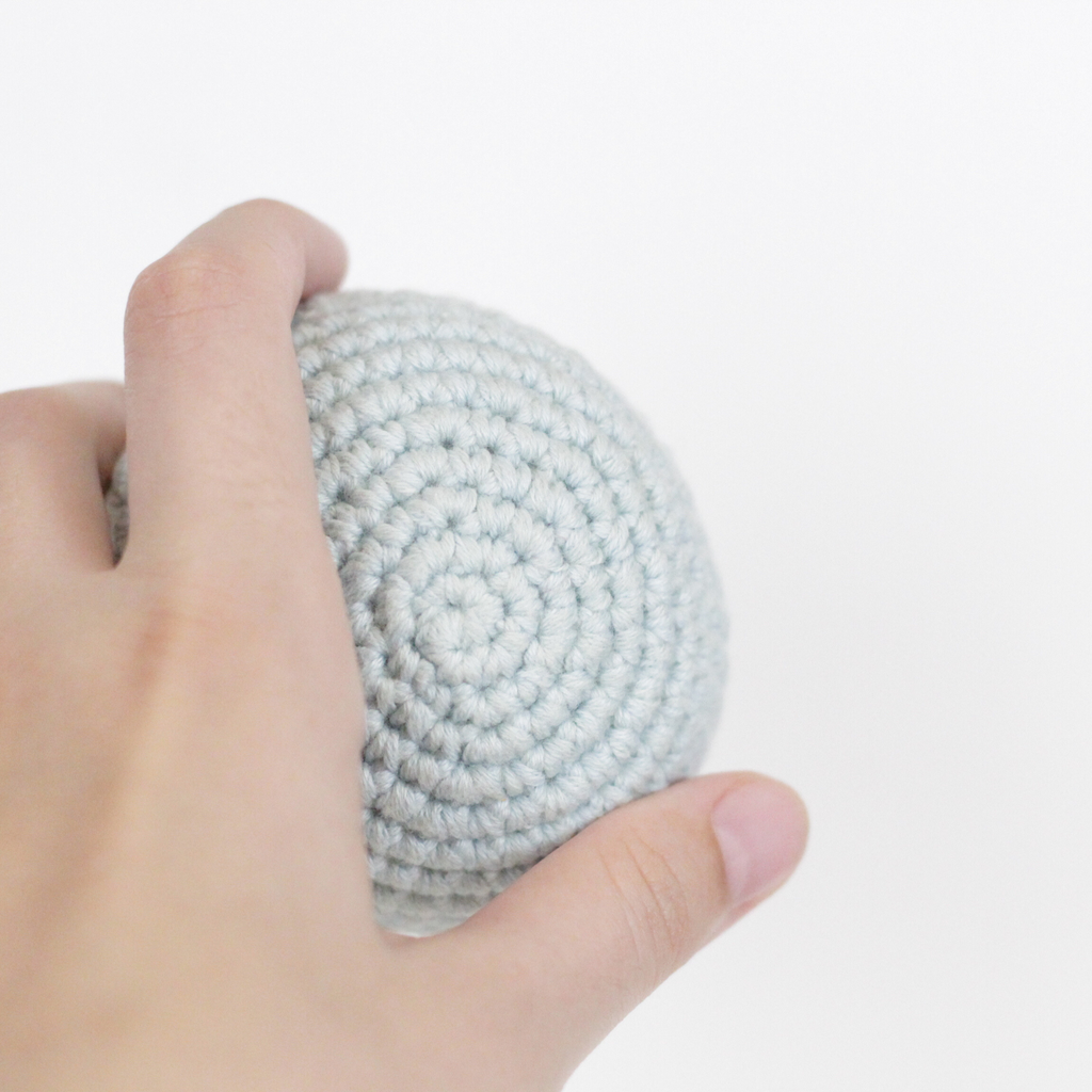 Hand holding a crocheted, ice blue ball. Handmade crochet dog toys from Lana Royals Pet Wear.