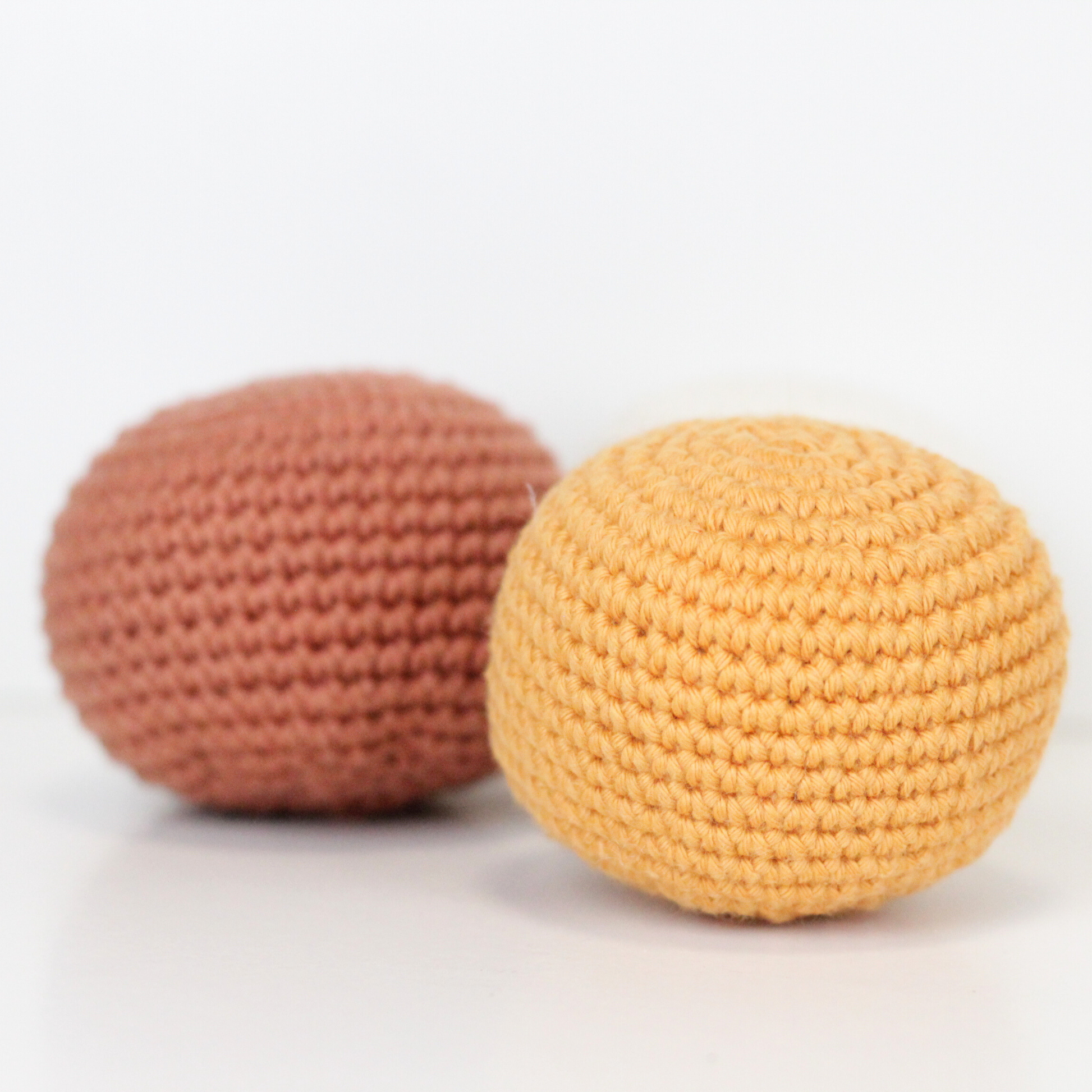 Three crocheted balls in white, rust orange, and apricot yellow. Handmade crochet dog toys from Lana Royals Pet Wear.