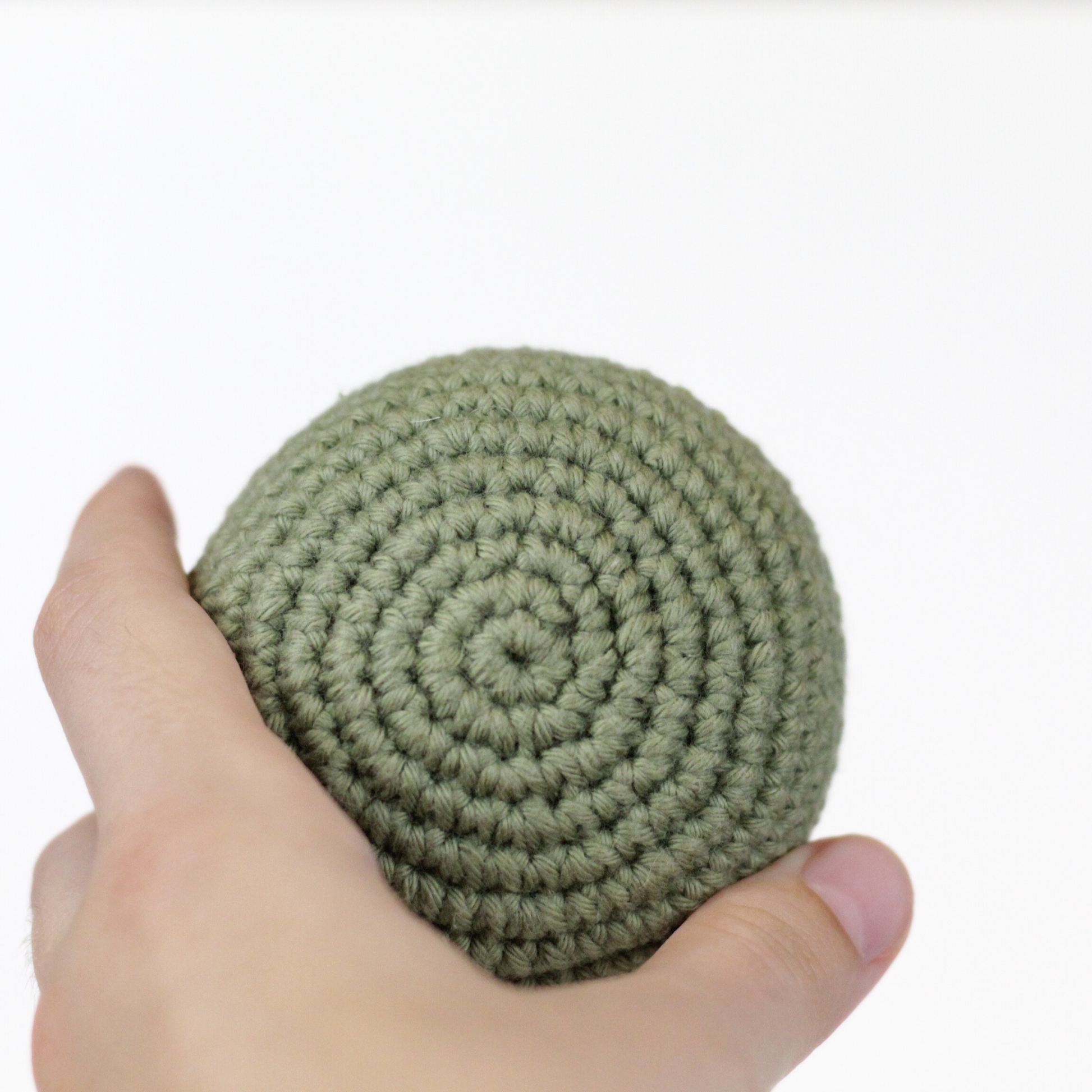 Hand holding an olive moss green crocheted ball. Handmade crochet dog toys from Lana Royals Pet Wear.