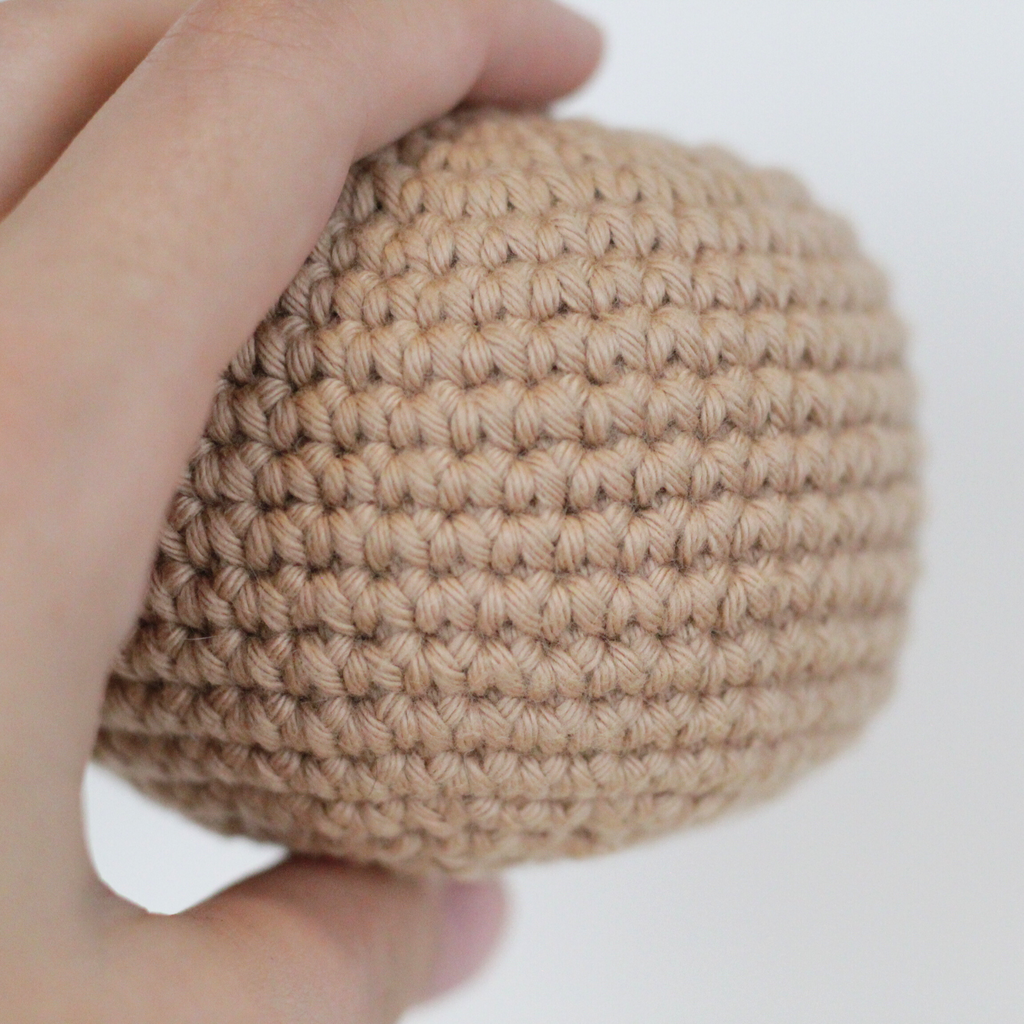 Hand holding a beige crocheted ball. Handmade crochet dog toys from Lana Royals Pet Wear.