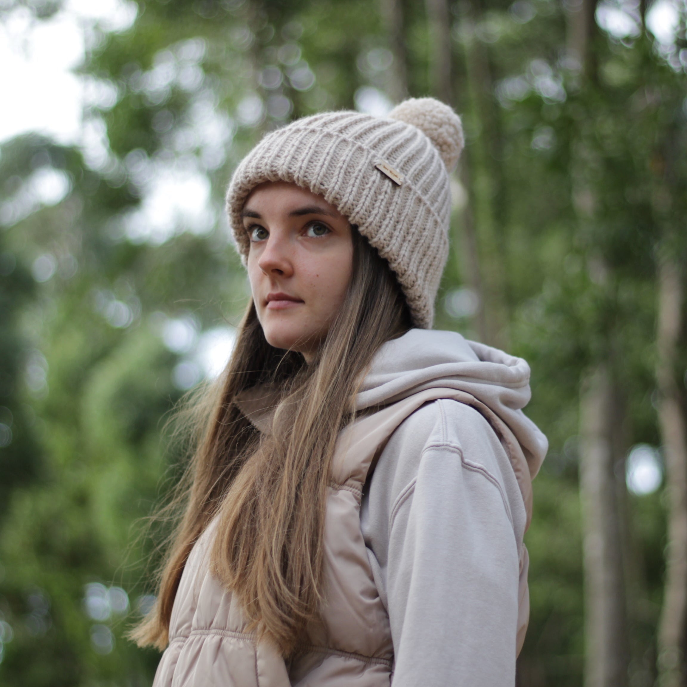 Woman wearing a beige handmade knit beanie hat with pom pom, from Lana Royals Pet Wear.