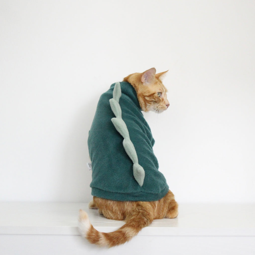 Ginger cat wearing a teal fleece jumper with aqua fleece dinosaur spikes costume add-on, custom-tailored to measure by Lana Royals Pet Wear.